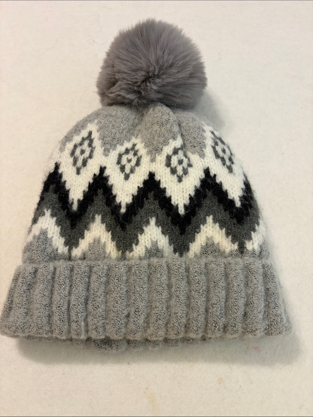 Gray knit beanie with a Fair Isle zigzag pattern and a fuzzy pom-pom on top.